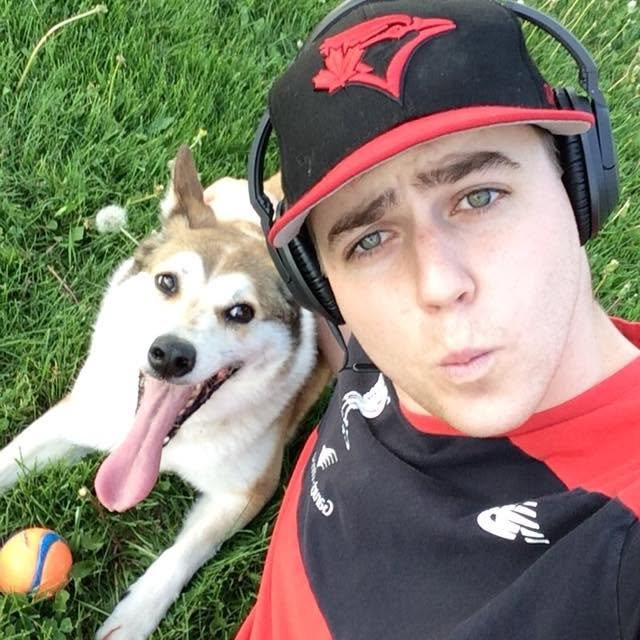 Alex in the grass beside the family dog, Jackie, wearing a ball cap and headphones